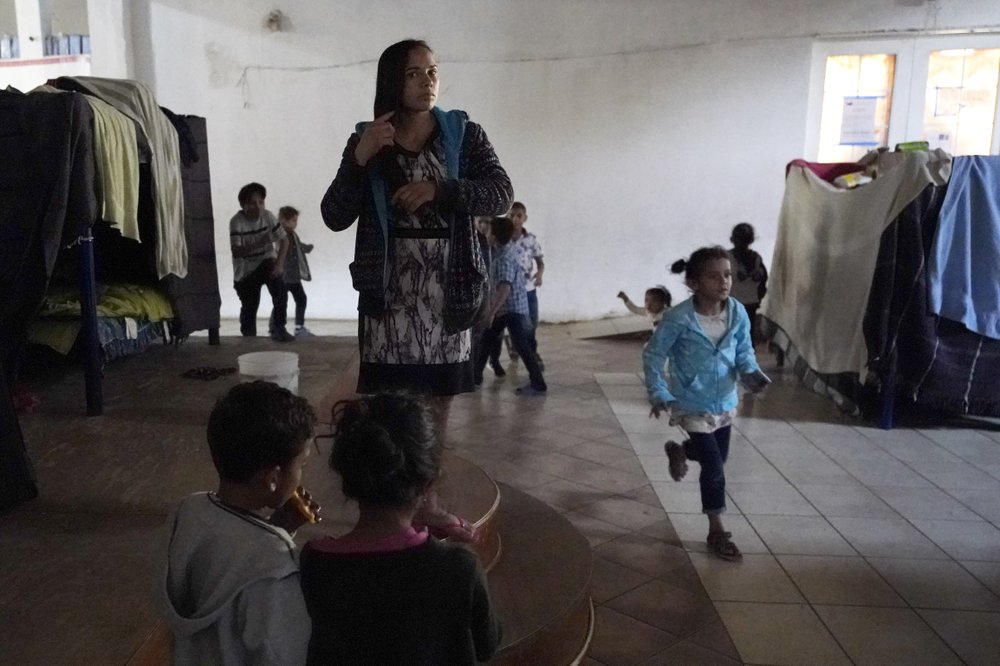 Una mujer hondureña que espera para entrar a Estados Unidos (al centro) se peina el 17 de febrero de 2021 mientras unos niños juegan cerca, en un albergue en Tijuana, México. (AP Foto/Gregory Bull)